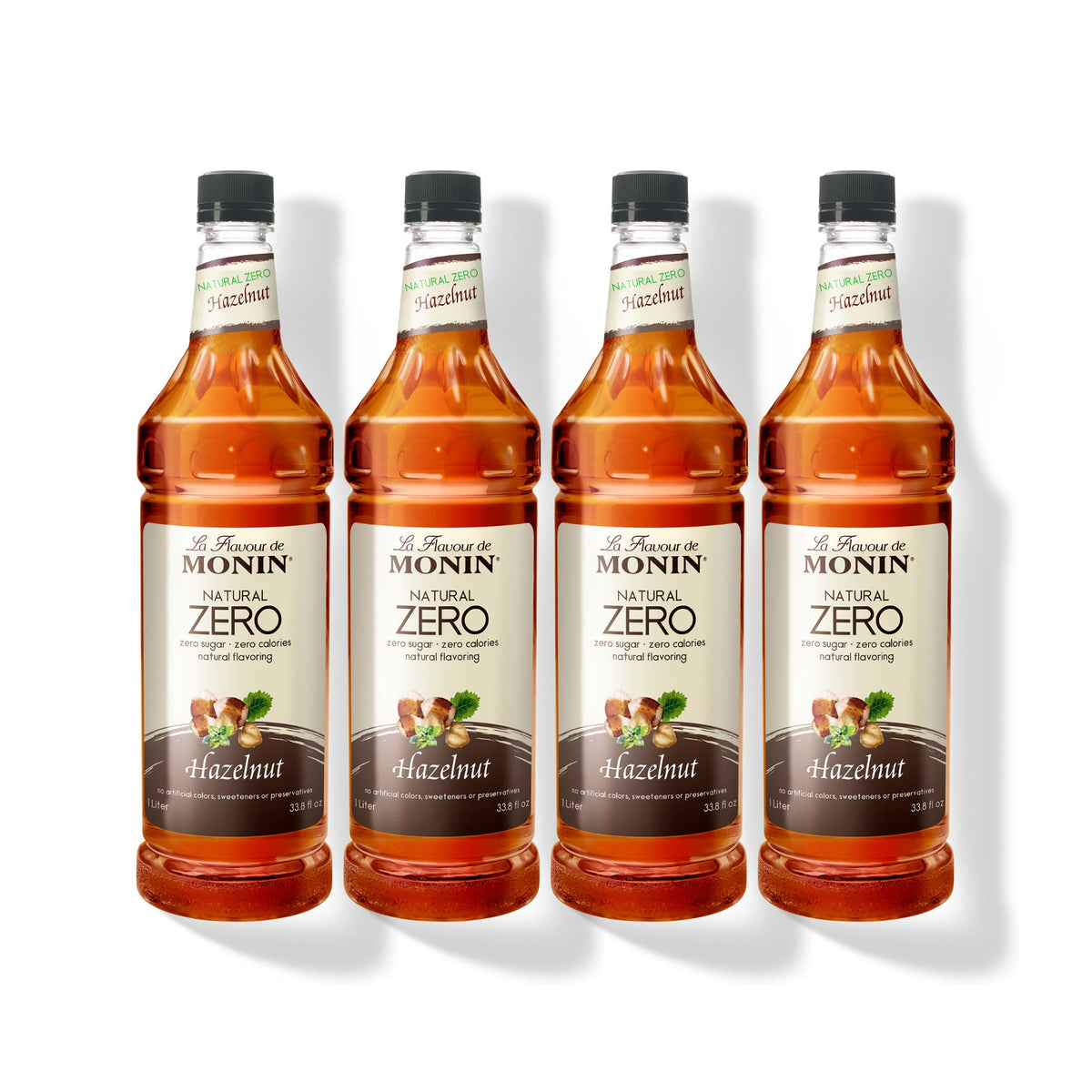 Four 1L plastic bottles of Monin Natural Zero Hazelnut syrup in a row